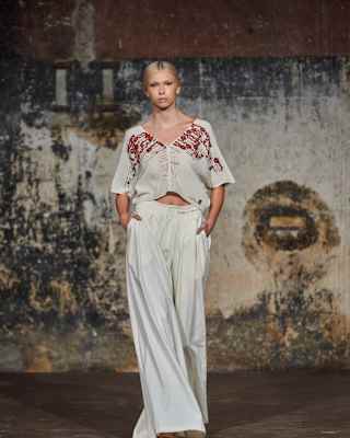 A blonde female model stands in an industrial setting in Collectiva Concepción white loose trousers and a top with red sequins.