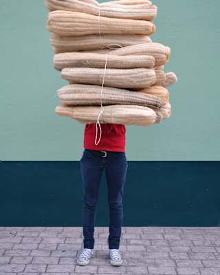 Mexican designer, Fernando Laposse stands by a mint-hued wall, holding a tied bundle of dried luffa, which obscures his face.