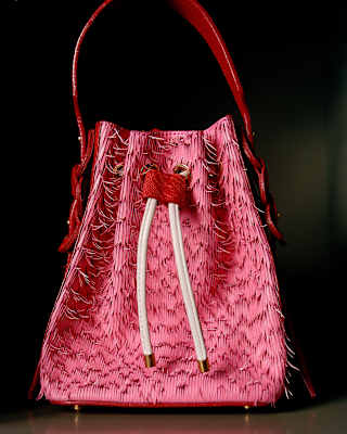 A tasselled pink bag with white pulls and a red shoulder strap by Viviers Studio stands out against a black background.