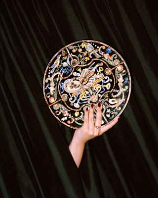 A hand holds an ornate plate decorated with birds and a violin, to commemorate Vanessa-Mae's garden concerts at Le Manoir.