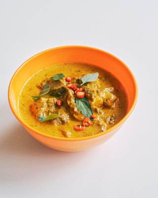 Close-up of Panang Curry with meat and slices of red chilli and curry leaves, served in a yellow bowl, seen from above.