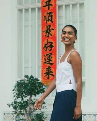 Kirthanaa Naidu, creative consultant, smiles to camera as she is photographed in a white top by an orange banner in Penang.