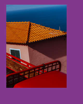 Artistic geometric image of a terracotta-roofed house with soft pink walls and ocean backdrop, seen over red railings.