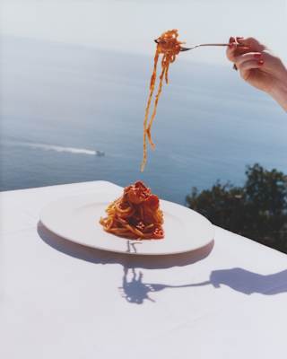 Image from the Liguria cookbook shows a bowl of three-tomato Spaghetti alla Elizabeth Taylor enjoyed at an ocean-view table.