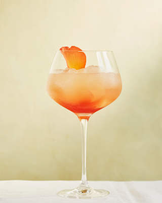 A rose petal garnishes a Portofino Spritz, which looks like sunset in a glass, with lemon juice, gin, rose liqueur and syrup.