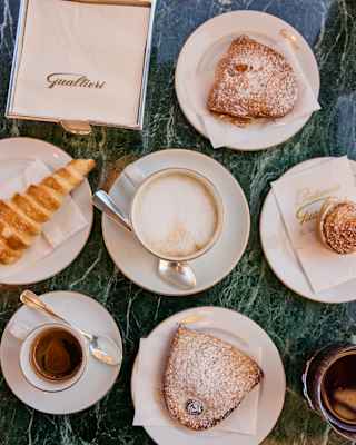 Looking down on a cappuccino and espresso with four plates of sugar-glazed pastries alongside a Gualtieri napkin dispenser.