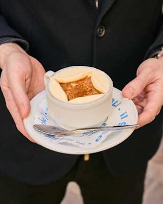 Two hands hold a cup of Affogato, where semi-circle scoops of ice-cream border a well of coffee, seen at Vivoli Gelaterria.