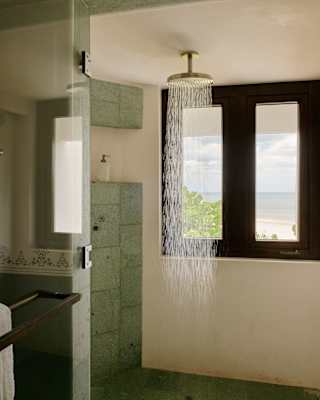 In an Ocean View Junior Suite bathroom, a refreshing monsoon shower runs in front of a window offering glorious sea views.
