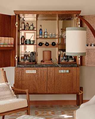 Bottles and apparatus for preparing cocktails adorn a mirrored teak drinks cabinet with cupboard doors and tiered shelving.