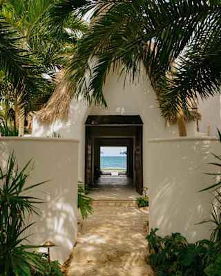 A garden path flanked by white walls and palm fronds passes through Villa Maroma and out onto the dazzling beachfront lawn.