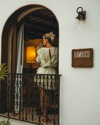 Bambuco's wood sign adorns the exterior wall by an open arched window where a blond woman in a white dress sips from a glass.