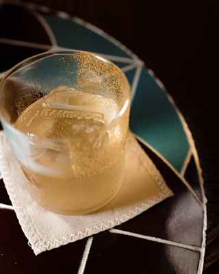 Close-up of Bambuco-branded ice cubes in a half-drunk cocktail in a tumbler set on a coaster on a tiled table top.