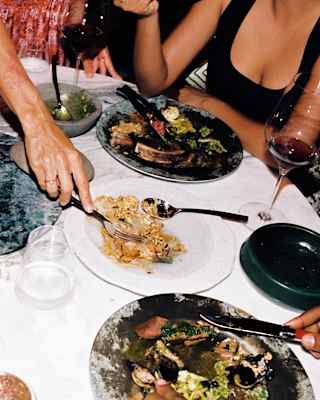 Looking down on table at Woodend restaurants, where a group enjoy vibrant dishes, and a guests reaches to serve from a dish.