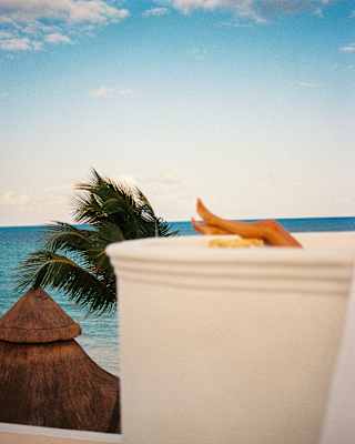 A sunbather rests her legs on the white wall of her ocean-view terrace, body obscured behind the curve of the wall.