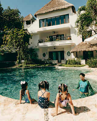 Three girls, seen from behind, sit on the edge of a pool looking at a staff member in a rash vest, who stands in the water.