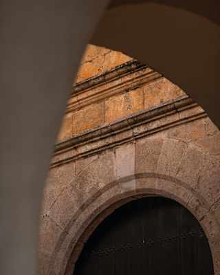 A honey-hued stone wall with an arch, viewed at an angle through a perpendicular archway.