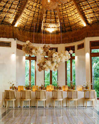 A dining table for twelve is ready for guests beneath decorative hanging pompoms and the high thatched roof of Palapa Tolok.