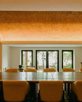 View over a table flanked by twelve yellow chairs into the Violoncello room, with mellow décor and rustic brick roof panel.