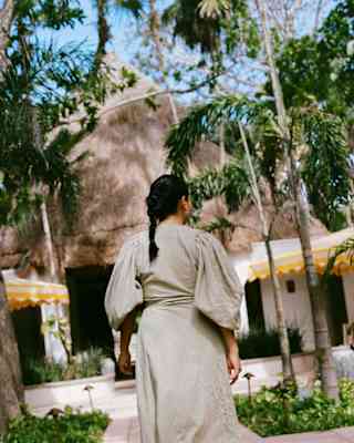 In sage uniform dress, a female member of staff with dark hair in a plait walks towards the hotel lobby, seen from behind.