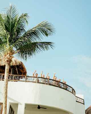 Six members of Maroma staff wave from the railings of an upper terrace, in a view that catches the blue sky and a palm tree.