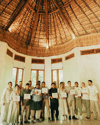 Beneath a high palapa ceiling, a group, mainly in cream attire, face the camera with papers certifying their work with Parley.