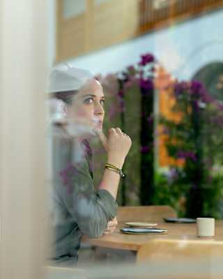 Chef Pía León looks pensive as she sits at a table, viewed from the outside through a window that reflects strips of sky.
