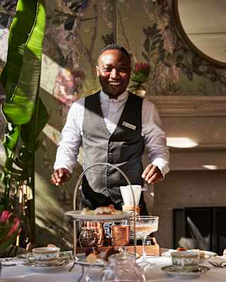 A member of staff smiles broadly as he prepares to clear a table after guests have enjoyed an afternoon tea.