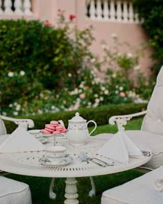 A pretty pile of pink macarons is a vibrant addition to an afternoon tea with crockery, napkins and garden table in white.