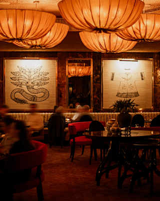 Large orange fabric pendant lights and backlit tapestries create a warm glow for diners, blurred by motion, in the Red Room.