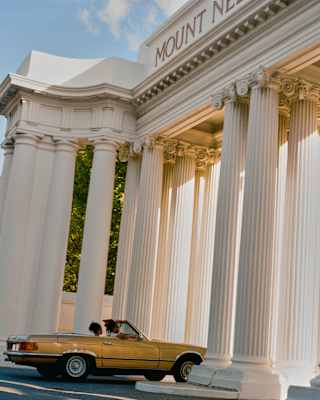 Two guests in a yellow convertible car pass through the spectacular, tall columns of the Mount Nelson Hotel's Royal Gateway.