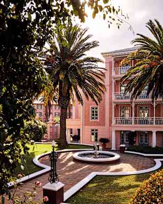 Hotel with pink walls and balconies overlooking palm trees and a fountain