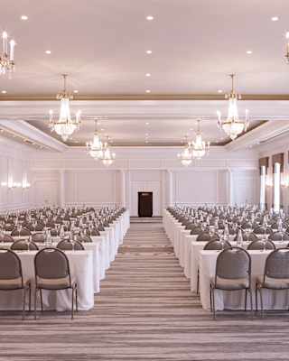 The bright Ballroom venue is prepared for an event, with rows of long white-clothed tables either side of a central aisle.