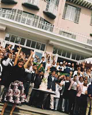 Angled image of staff gathered on the steps outside the Mount Nelson Hotel, celebrating its 125th year with a large cake.