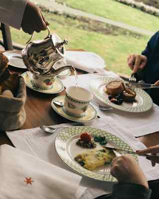 Angled close-up of a waiter pouring water from a silver pot into a cup at a table where two diners enjoy an al-fresco meal.