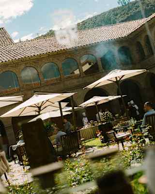 Angled image of the courtyard, where guests sit beneath parasols in the sun-drenched gardens, seen through a window.