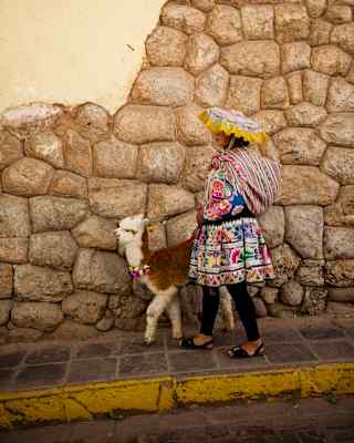 A lady wearing traditional clothing, standing near an alpaca in Cusco