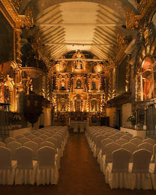 White-clothed chairs await a ceremony in the serene San Antonio de Abad Chapel, ornate with illuminated original artworks.