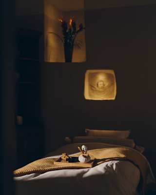 A small wooden tray with a scent sticks and herb pot rests on a mustard throw on a bed in a low-lit room at the spa.
