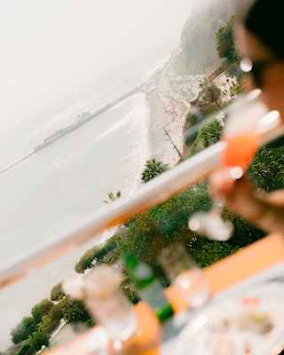 Angled image of a guest sipping a tall cocktail in soft-focus foreground, overlooking the dramatic coast of Lima.