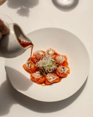 A jug pours sauce from a jug over a dish of pink salmon, arranged around a ball of shredded salad vegetables at Tragaluz.