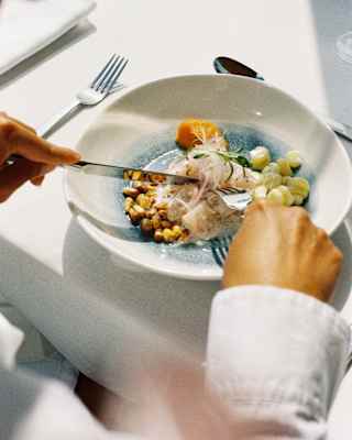 A guest cuts into a classic ceviche dish at Tragaluz, with onions, sweet potato and fresh corn, seen over a diner's shoulder.
