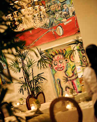 Tilted view of Mateo Liébana's lively murals, seen over candlelit dining tables in soft-focus foreground at Tragaluz restaurant.