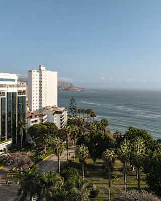 The white and glass edifice of Miraflores Park rises above the palm trees of Parque Domodossola, facing the Pacific Ocean.