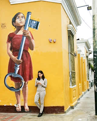 A woman looking at her phone, leaning against a yellow wall in Barranco, Lima