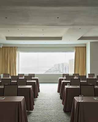 A wide Salón Pacifico window reveals the venue's incredible coast views, seen over eight brown-clothed tables with chairs.