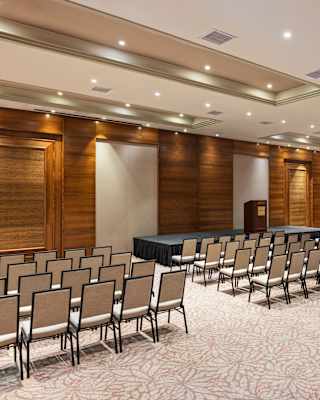 Chairs, grouped in columns, face the stage in the Copacabana meeting room, lit with glowing spotlights, seen from behind.