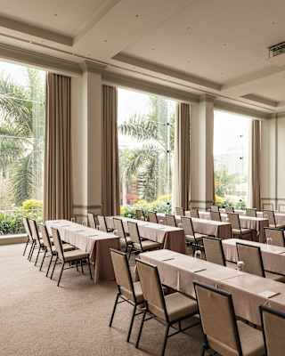 Three tall windows spill light into Salón Park, where ten long beige tables, each seating four chairs, face the front.