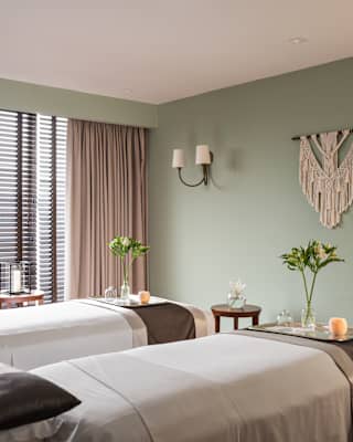 View into a pastel green treatment room with grey-pink curtains and twin beds with white sheets and brown throws.