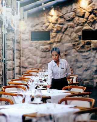 A waitress places polished glasses on white-clothed tables lining a wall of full length windows at elegant Tampu Restaurant.