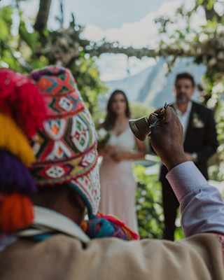 A shaman rings a hand bell before a bride and groom during an Andean ceremony to renew wedding vows, seen from behind.